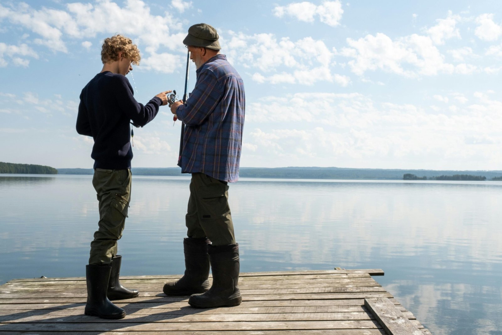 Grandfather and grandson fishing together on a tranquil lake dock, sharing moments and techniques.