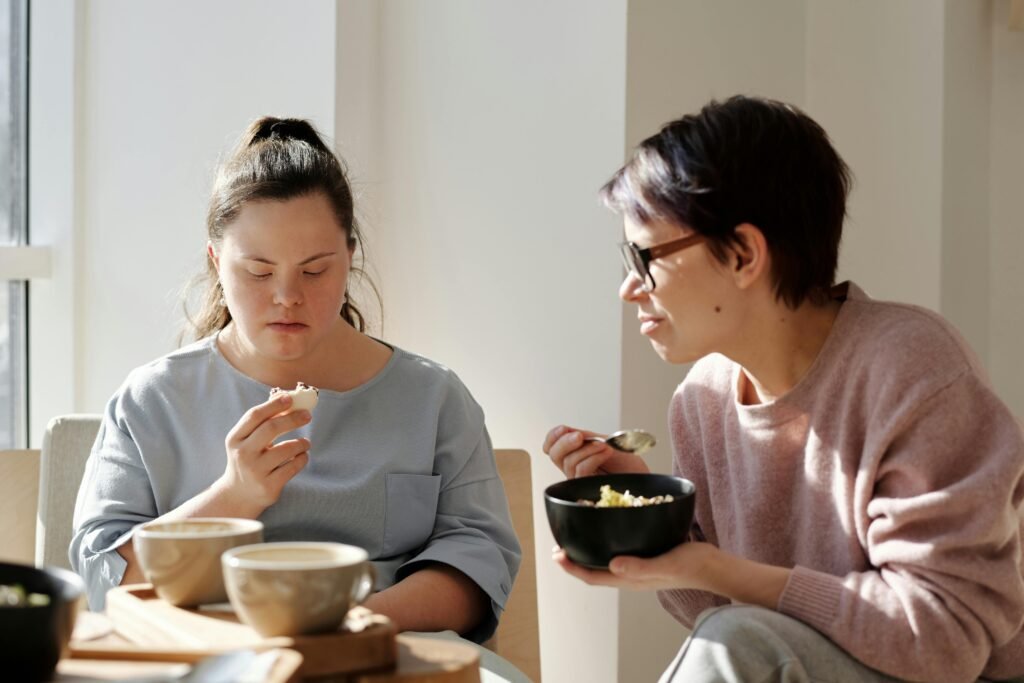 Two women sharing breakfast, one with Down syndrome, fostering togetherness and care.