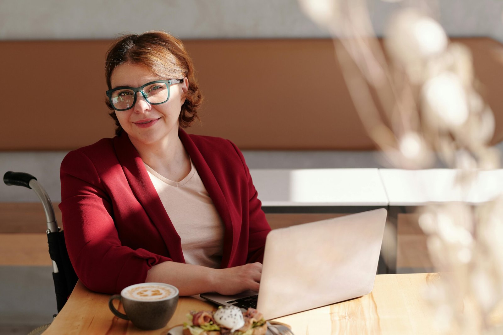 Smiling woman in red blazer using a laptop at a café table, enjoying her workday.