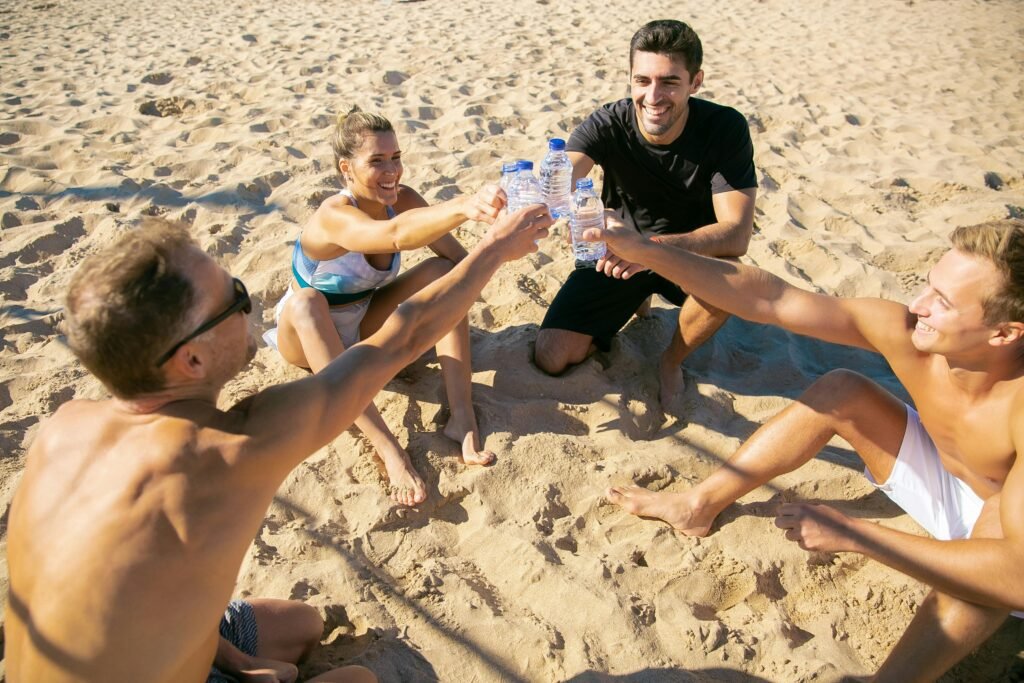 Group of friends enjoying a sunny beach day, cheering with water bottles, expressing happiness and togetherness.