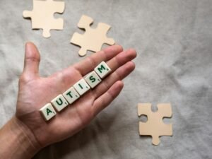 Hand displaying 'autism' spelled with scrabble tiles, accompanied by puzzle pieces, symbolizing autism awareness.